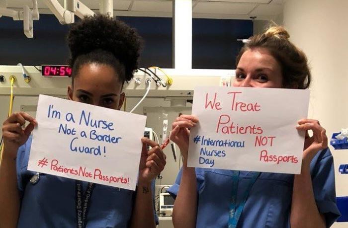 Nurses holding signs that say "We treat patients, not passports"