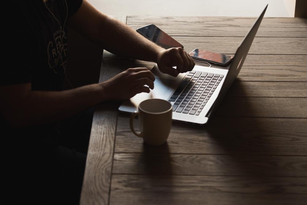 Hands on a laptop keyboard next to a cup of coffee, screen is hidden