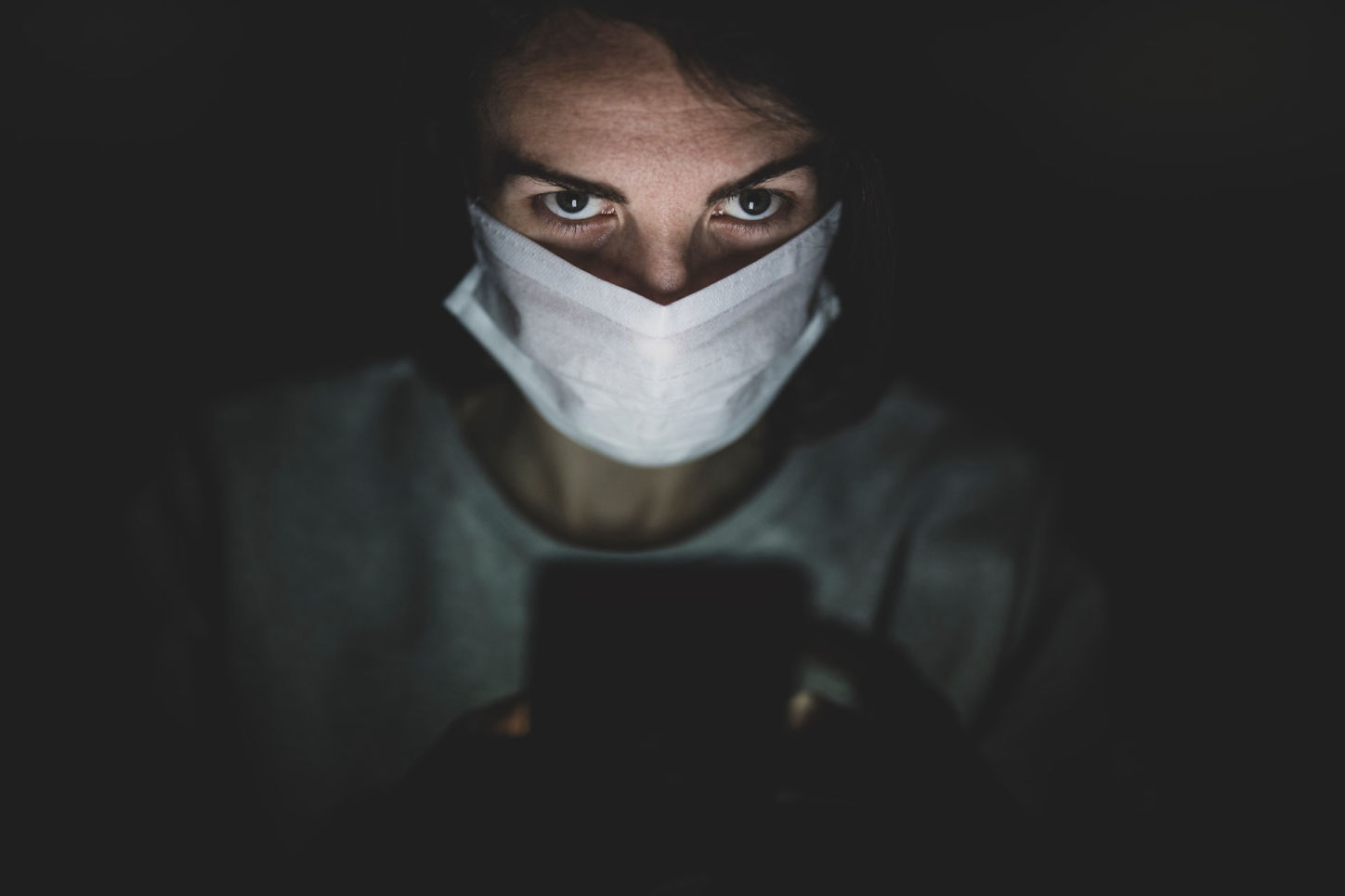 person wearing mask in the dark looking at phone