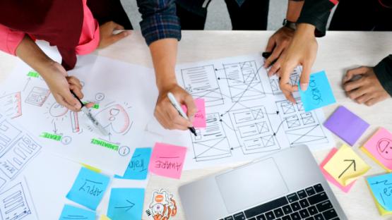 People planning an online resource on a desk with pens and paper