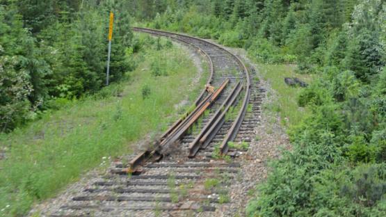 The end of a train track in a forest, with piled up sleepers, rails and ties