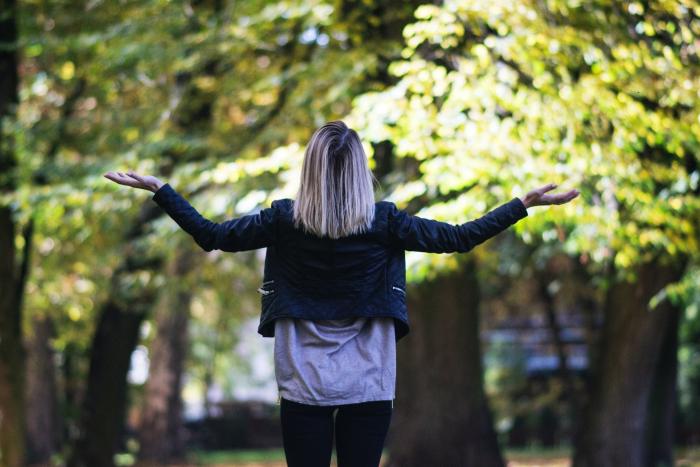 The back of a woman shrugging facing trees in daylight