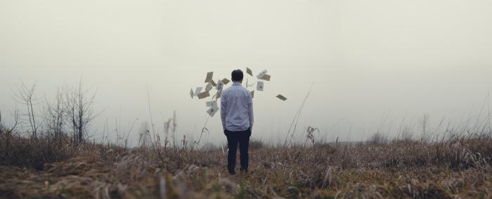 Man brack to the camera, in a landscape, looking at pages flying in fronts of him