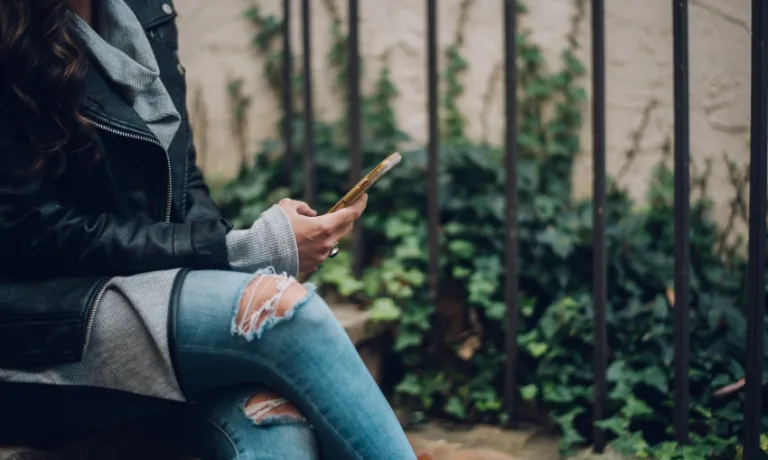 A woman sat on outside steps using a gold smartphone
