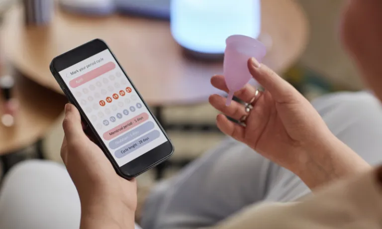 Someone holding a menstrual cup and looking a generic period tracking app