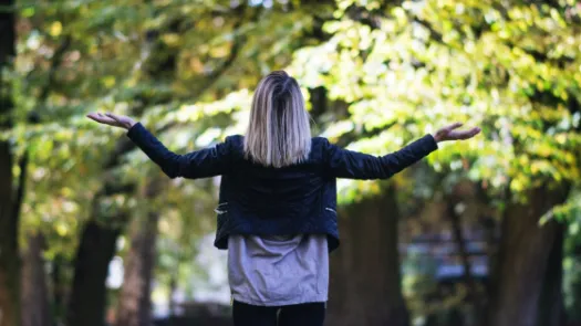 The back of a woman shrugging facing trees in daylight