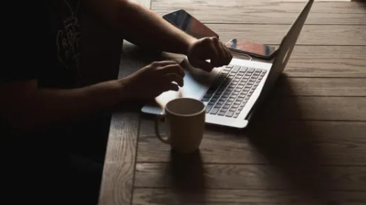 A person typing at a computer on a wooden table.