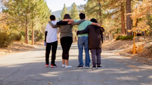 Four friends looking down a road with their arms around each other.