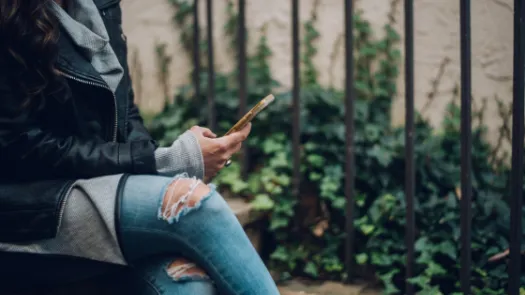 A woman sat on outside steps using a gold smartphone