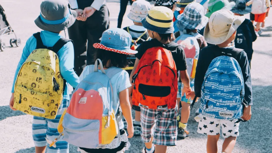 Young children walking to school hand in hand wearing colourful backpacks