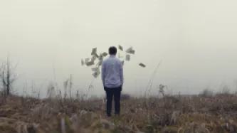 Man brack to the camera, in a landscape, looking at pages flying in fronts of him